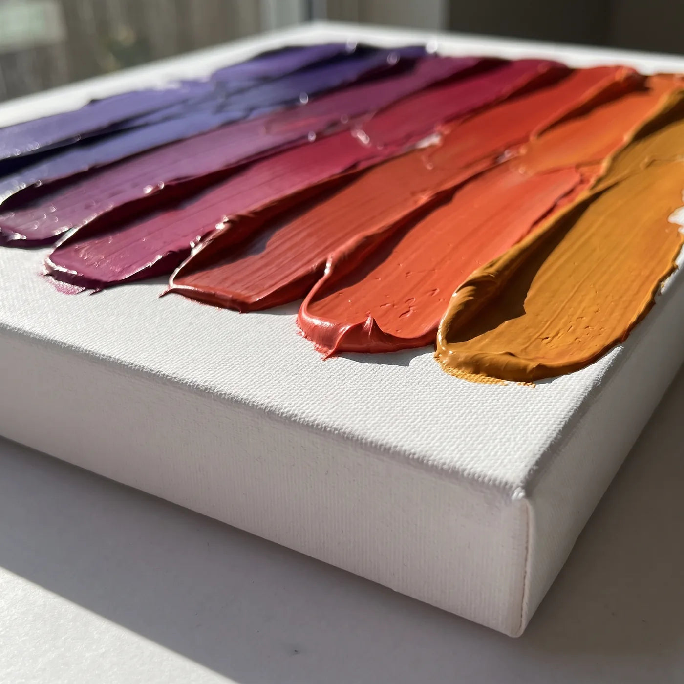 Hrana plátna 3D z boku — biely bok s hĺbkou 4 cm a pásy hustej akrylovej farby nanášané špachtľou, každý v inej farbe, spolu tvoriace prechod od fialovej po jantár